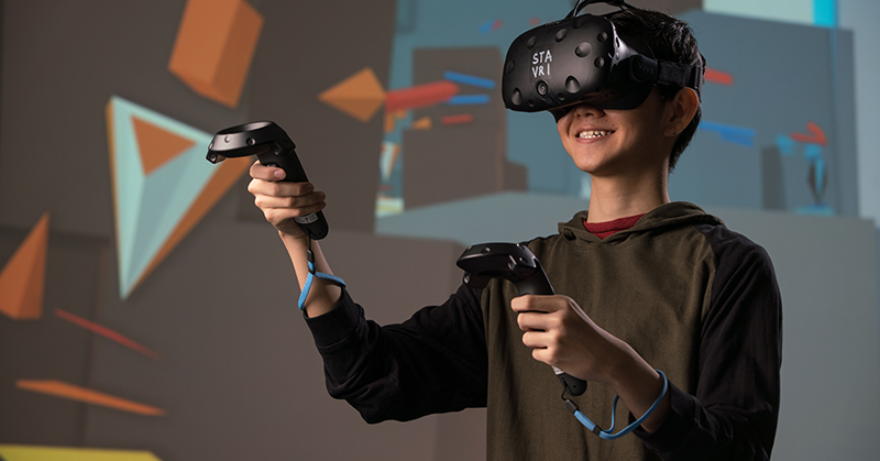 Person wearing VR headset and holding two VR triggers in their hands.