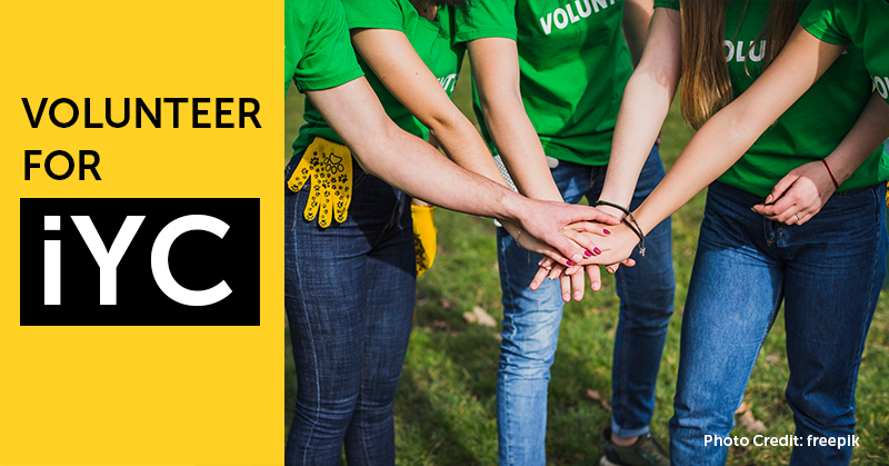 Bold black and white text with yellow background says, ‘volunteer for iYC’. 5 hands reaching into the centre of a circle, each hand placed on top of each other, as five people huddle in as one team.